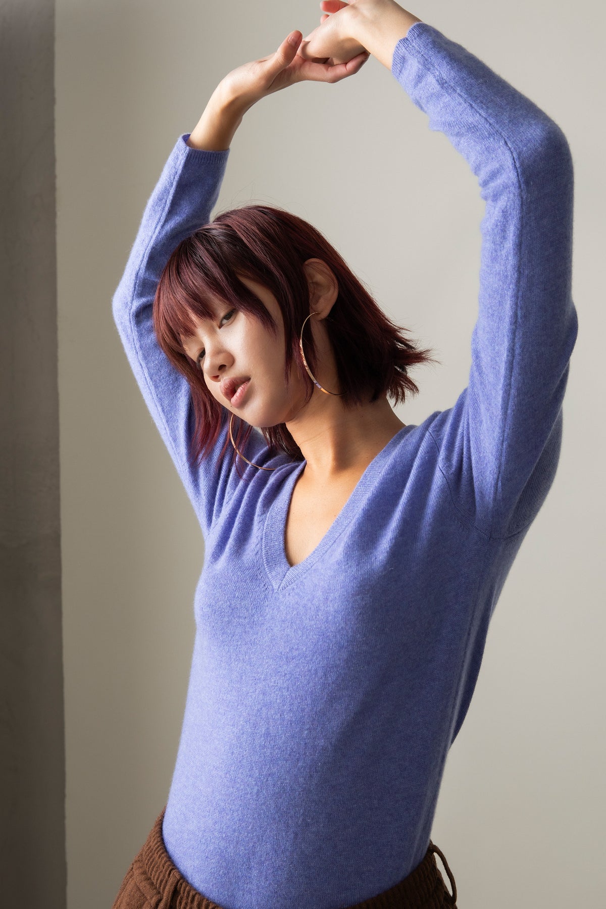 Model with arms raised showing the relaxed fit and deep V-neckline of the Women's Cashmere V Neck Jumper in Wisteria