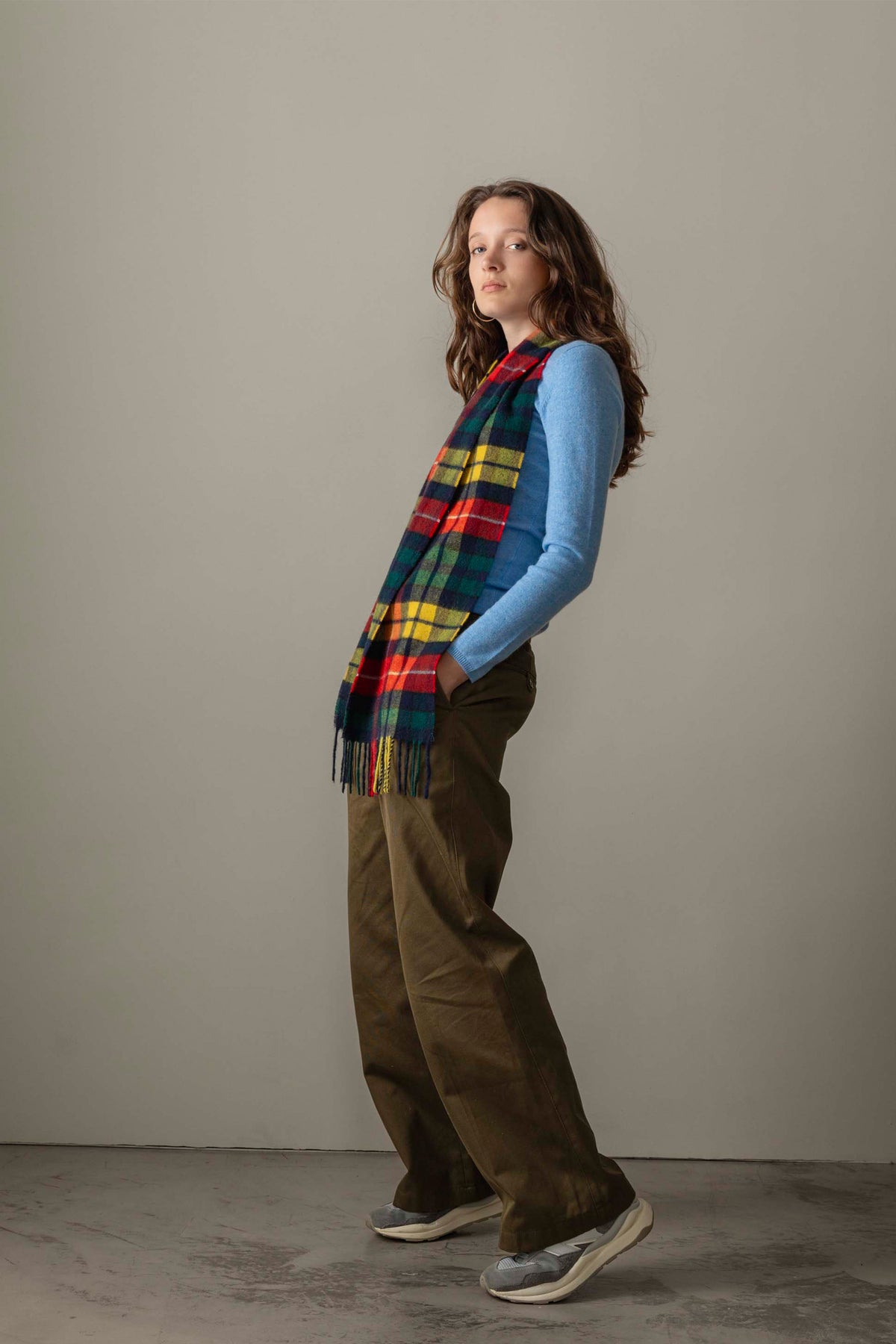 Side profile of model wearing the Women's Cashmere Crew Neck Jumper in Glacier blue, paired with a plaid scarf and olive trousers