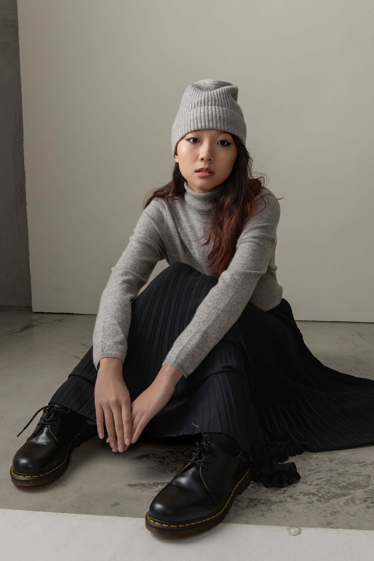 Women's Cashmere Polo Neck Jumper in light grey styled with a matching ribbed beanie, black pleated skirt, and black boots