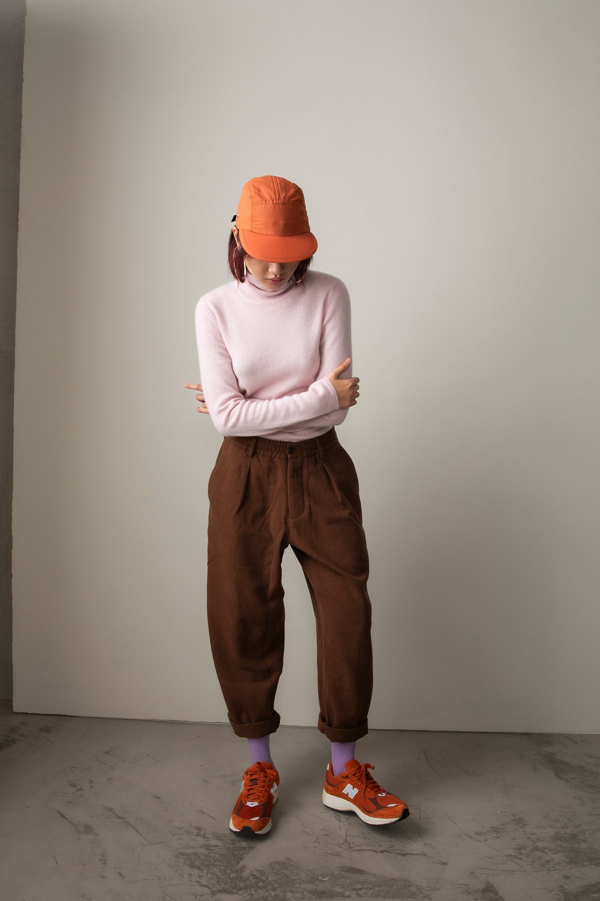 Women's Cashmere Polo Neck Jumper in Pale Lilac styled with brown pleated trousers, orange cap, and orange sneakers