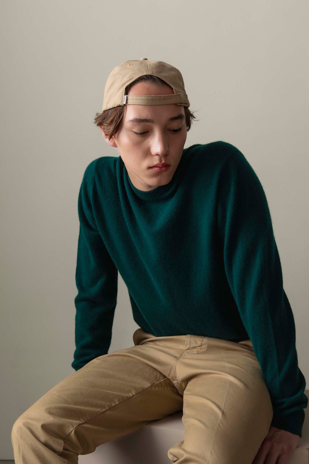 Model seated wearing Men's Cashmere Crew Neck Jumper in Richmond Green, showing soft texture and relaxed fit with khaki trousers