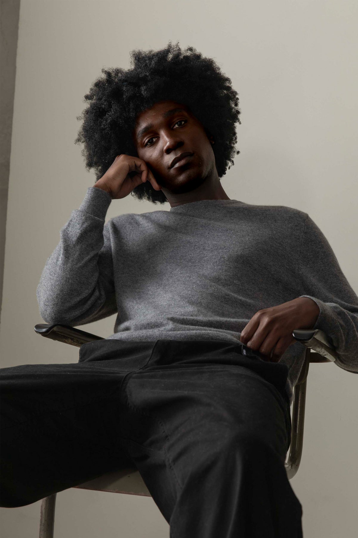 Model seated in chair wearing Men's Cashmere Crew Neck Jumper in Derby Grey, showing relaxed fit and soft knit texture
