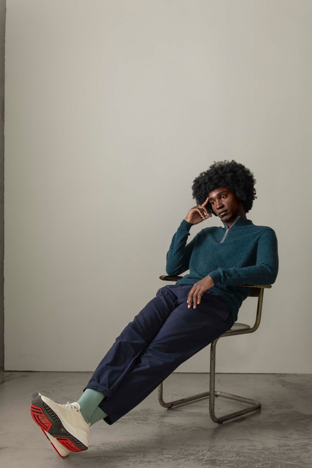 Model seated in chair wearing the Men's Half Zip Jumper in teal green, showing the relaxed fit and quarter-zip collar detail