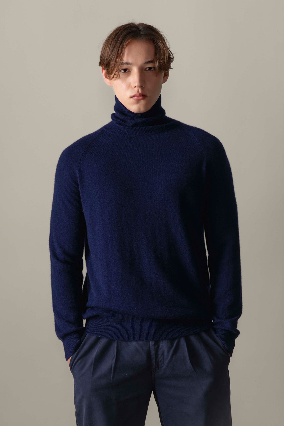 Model wearing Men's Cashmere Roll Neck Jumper in navy, front view showing the soft knit texture and slim fit