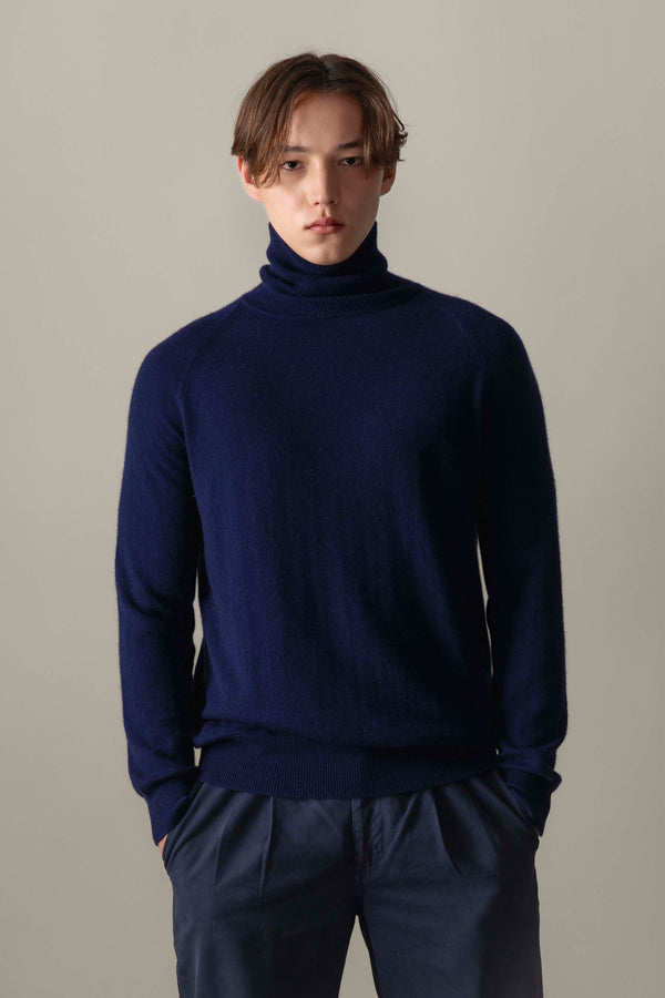 Model wearing Men's Cashmere Roll Neck Jumper in navy, front view showing the soft knit texture and slim fit