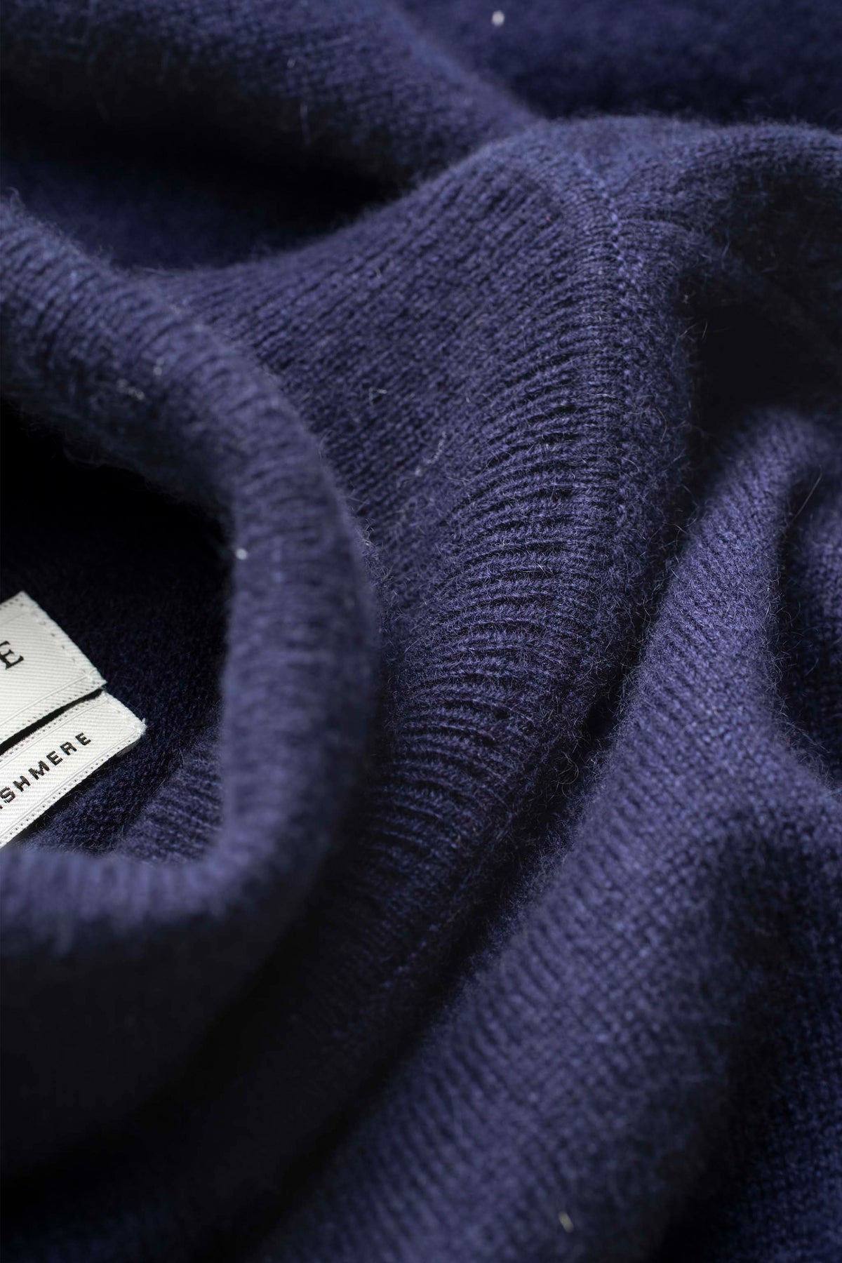 Close-up of the soft cashmere knit texture on the Men's Cashmere Roll Neck Jumper in navy, with brand label visible