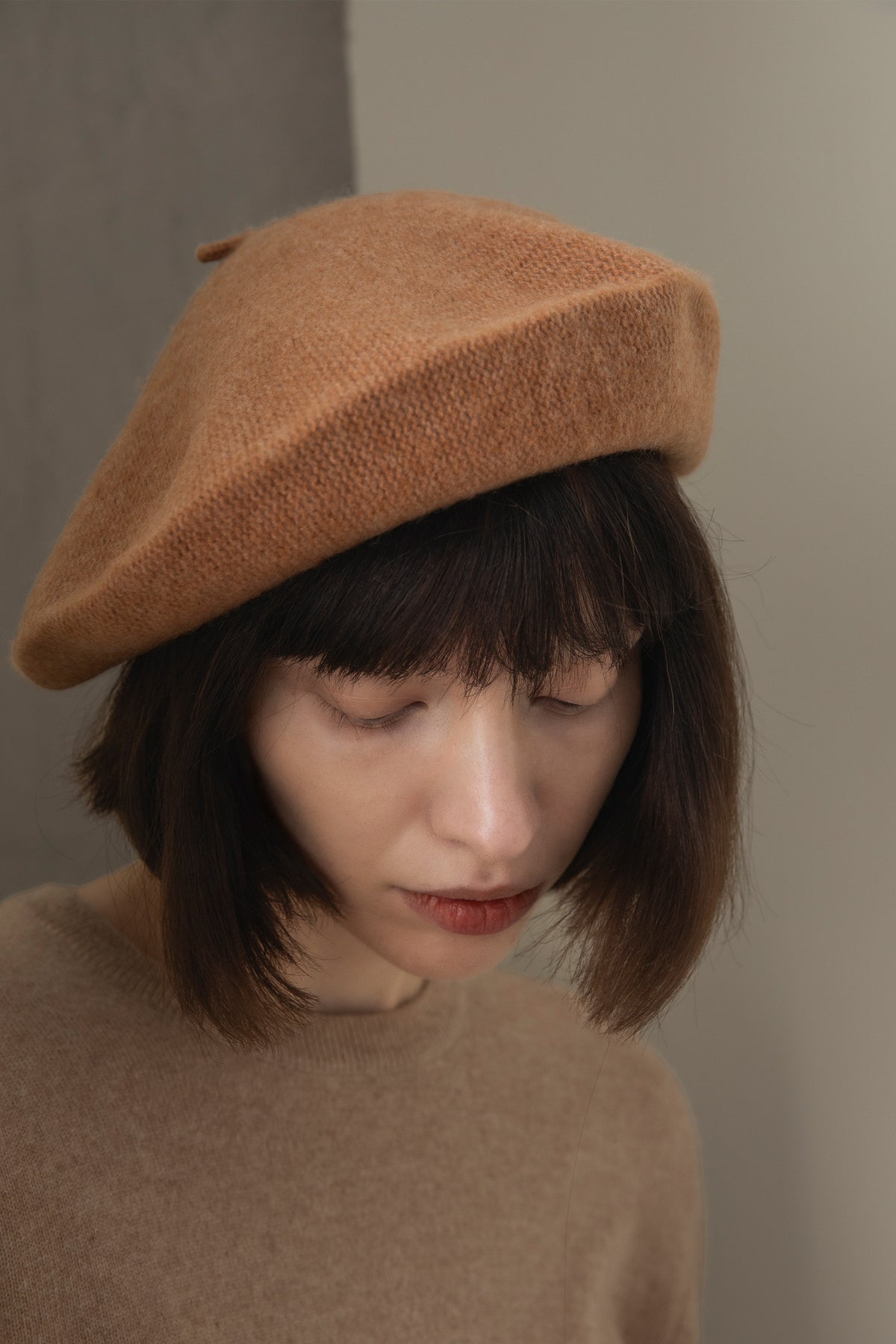 Cashmere Knitted Beret in Camel worn by model looking downward, showing the textured knit and slouchy silhouette