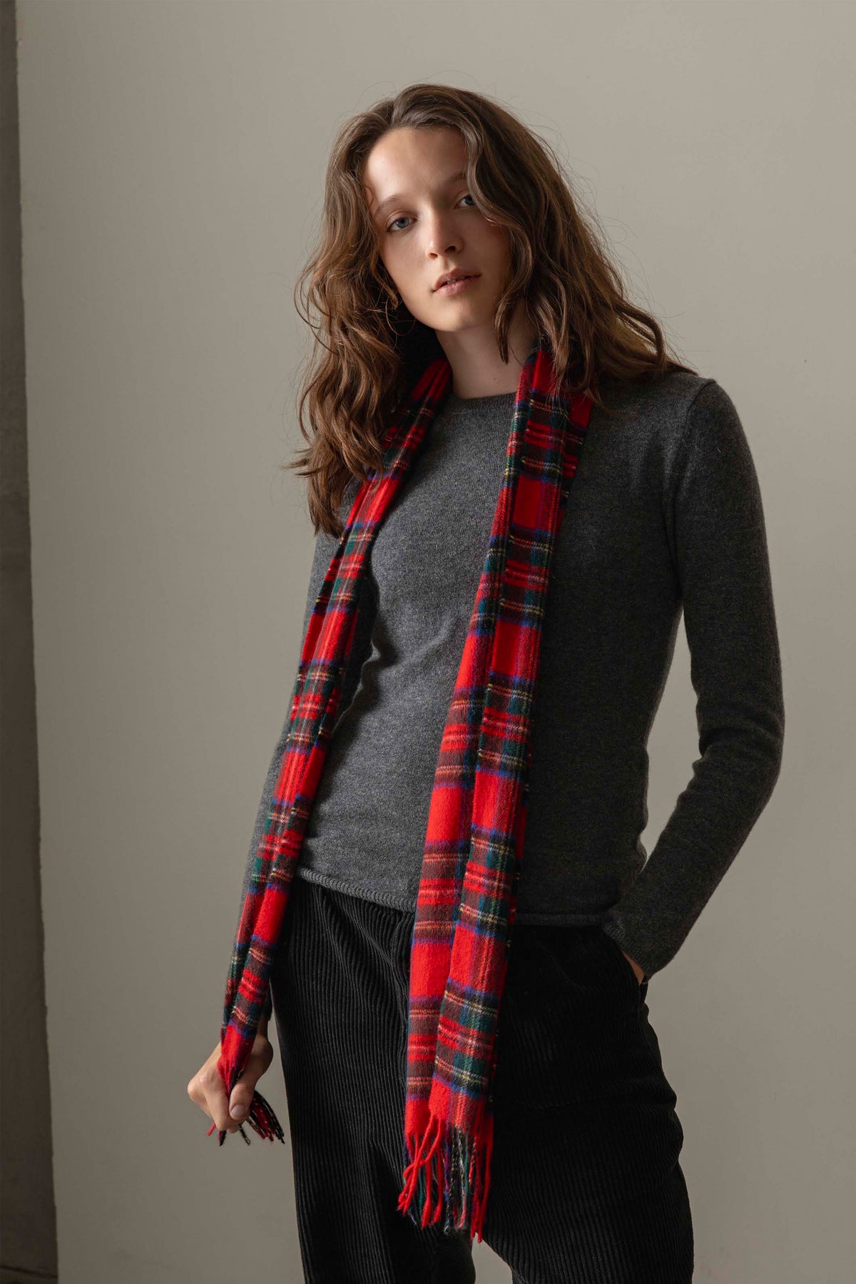 Made In Scotland Heritage Cashmere Scarf in Official Royal Stewart red tartan plaid, worn draped over a grey sweater with fringed ends