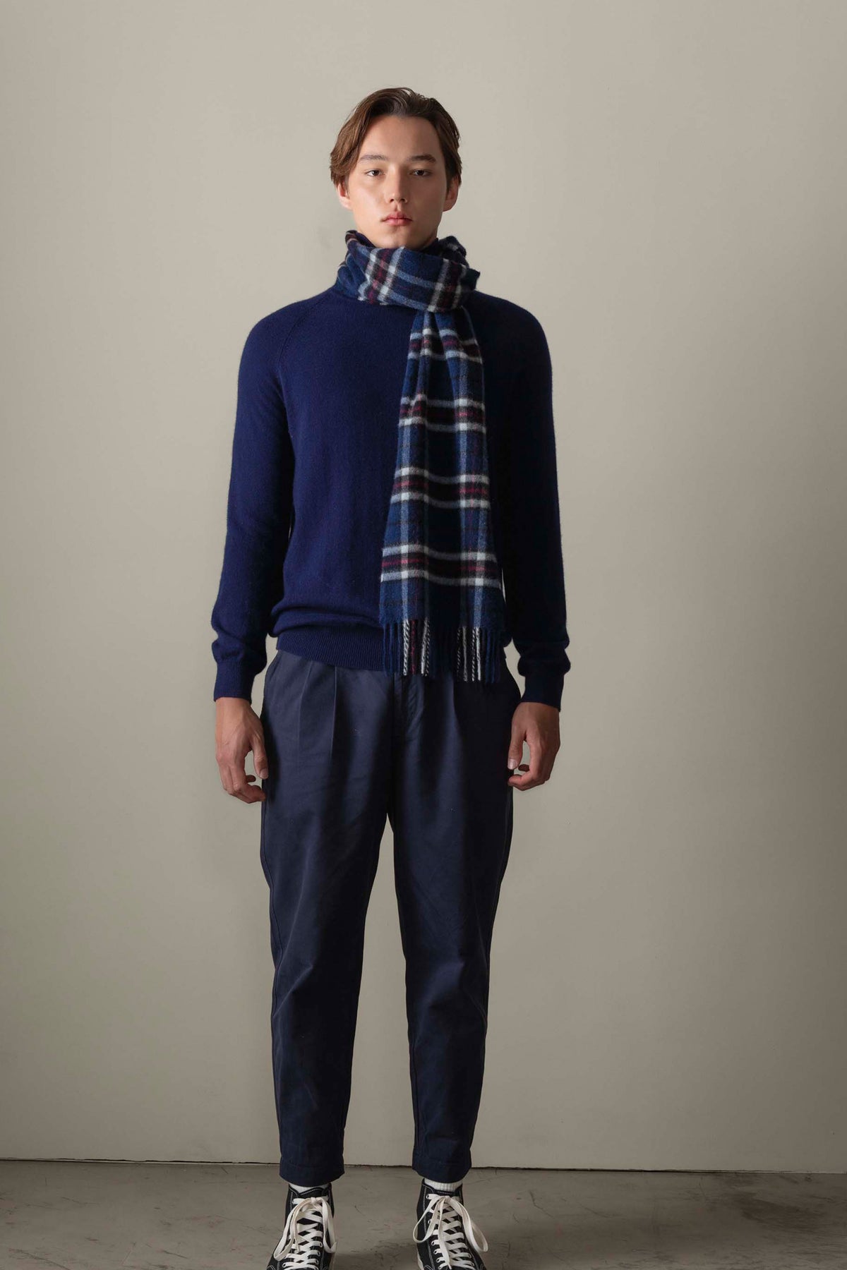 Made In Scotland Scotty Thompson Cashmere Scarf in Navy, blue plaid with white and red stripes, worn draped over a navy sweater