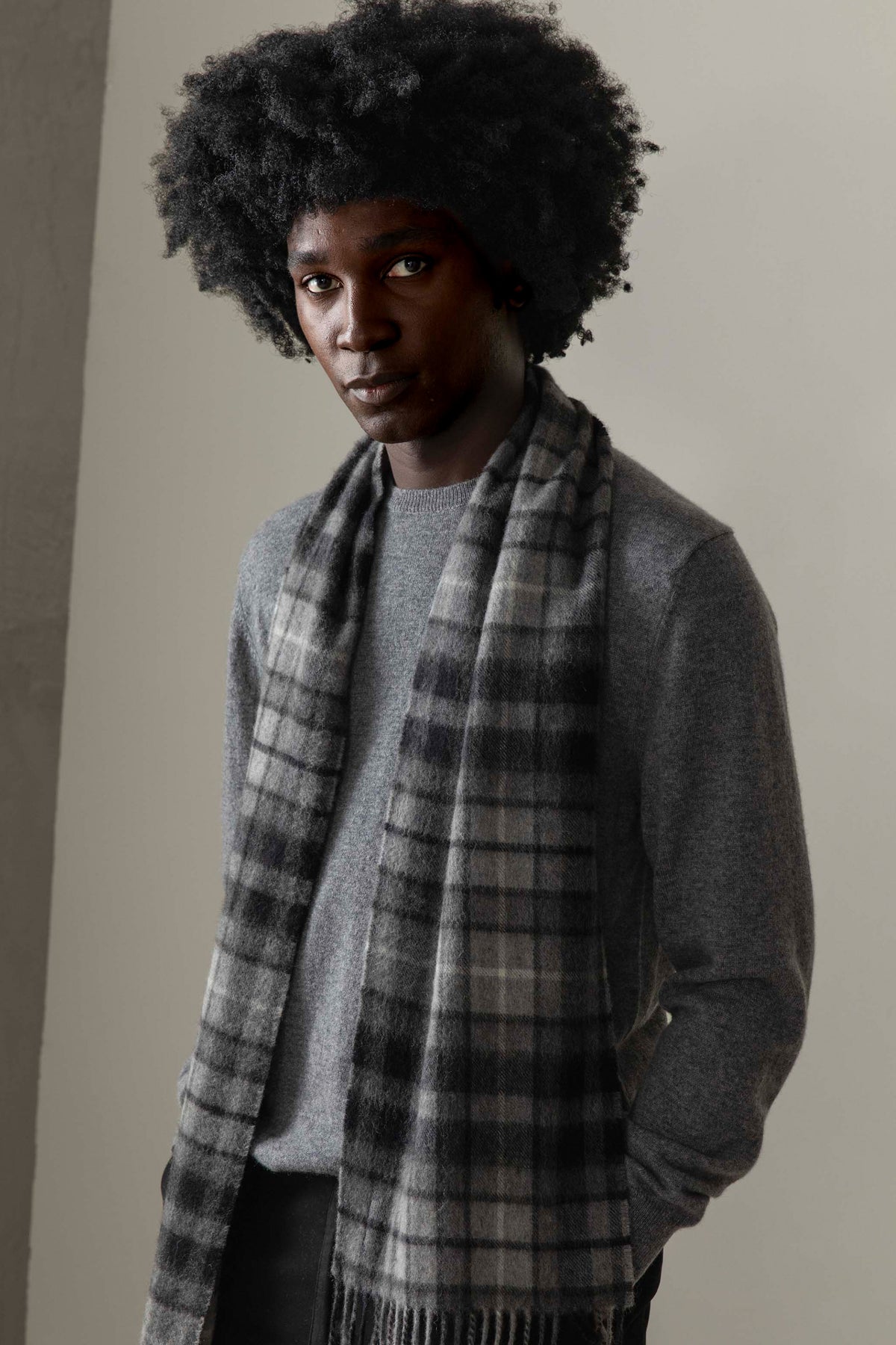 Made In Scotland Heritage Cashmere Scarf in Buchanan Grey plaid pattern, worn draped over a grey sweater showing the soft fringe detail