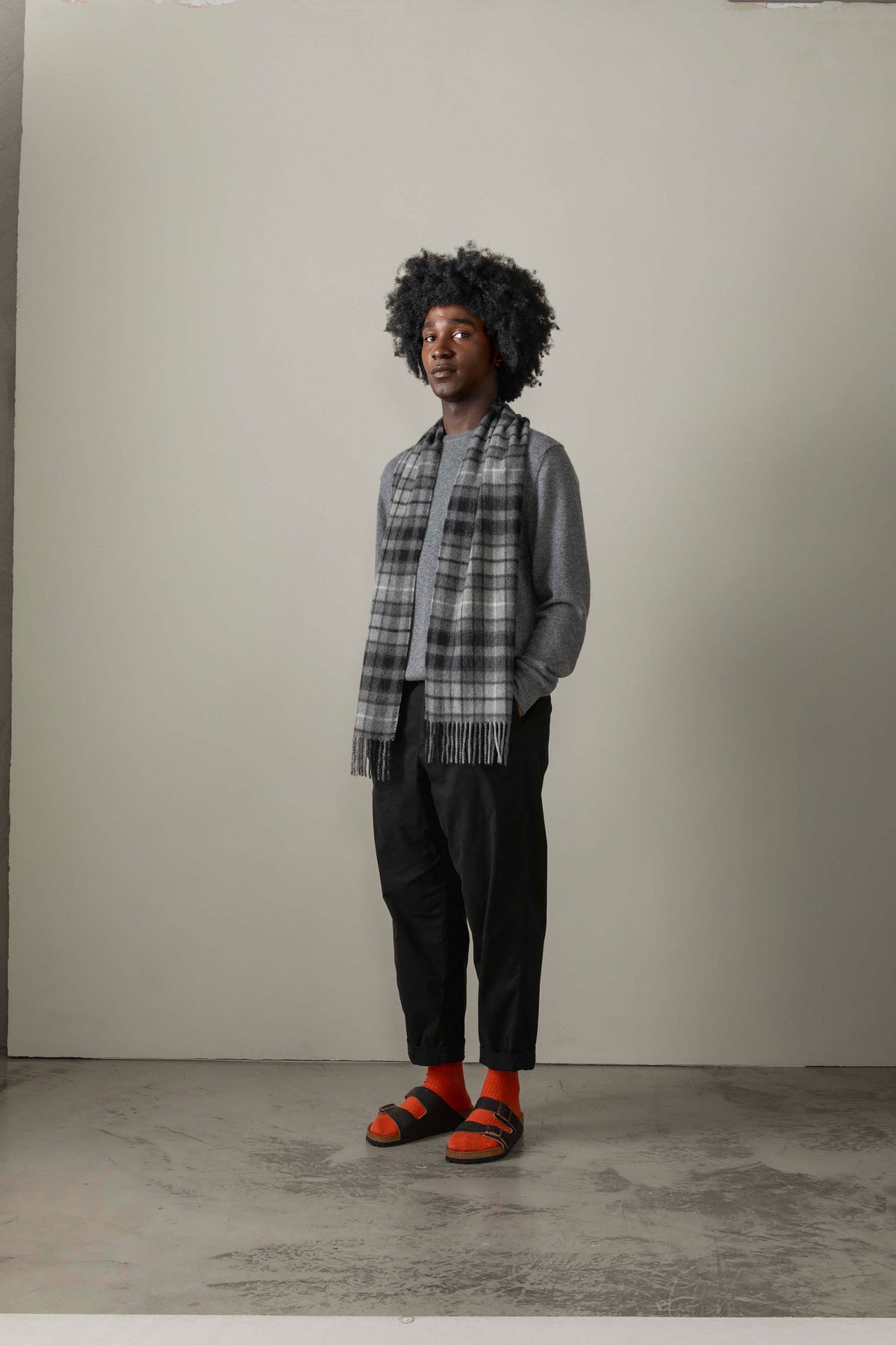 Model wearing Buchanan Grey Heritage Cashmere Scarf draped over a grey sweater, showing the plaid pattern and fringed ends