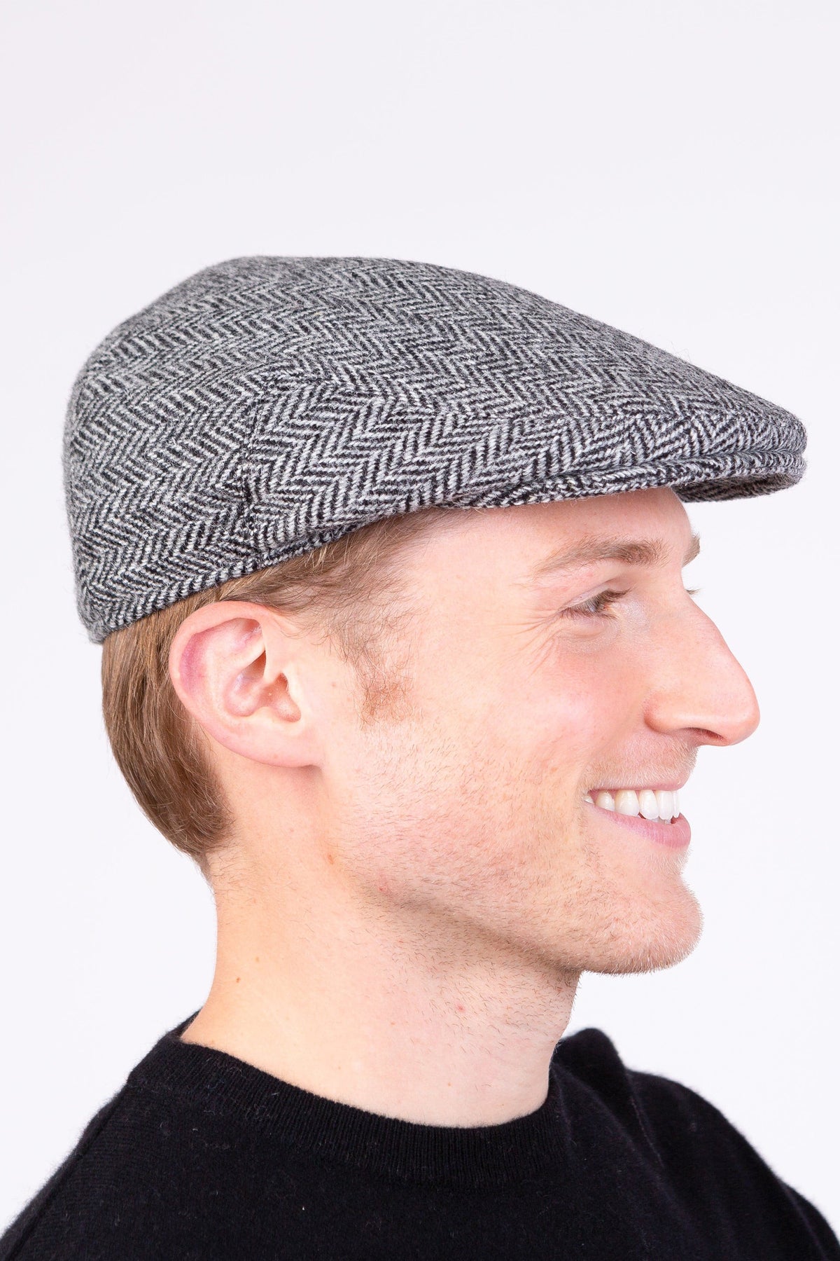 Harris Tweed Stornoway Cap in light grey herringbone worn by model, side profile showing flat cap shape and brim