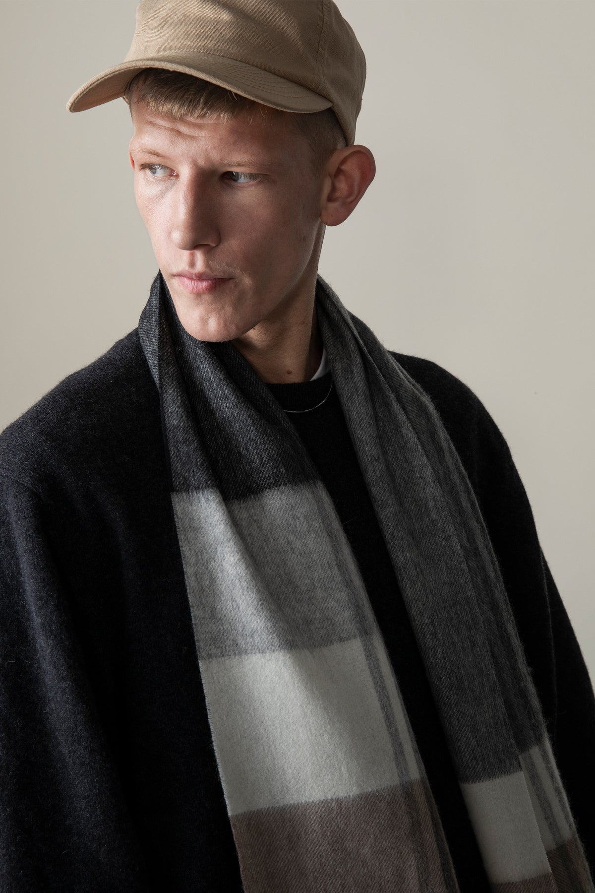 Model wearing the Contemporary Check Lambswool Scarf in Monochrome draped over a black coat, showing the grey and black check pattern