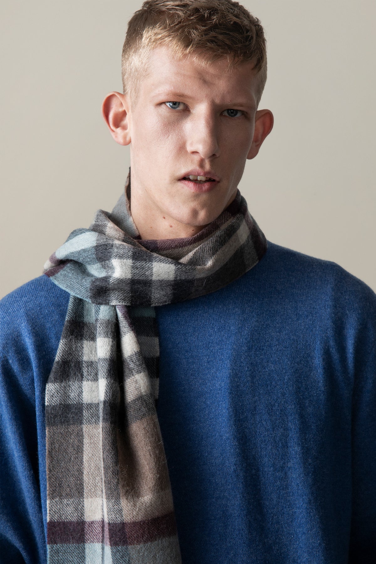Tartan 2 Lambswool Scarf in Blue Taupe worn loosely knotted over a blue sweater, showing the check pattern drape