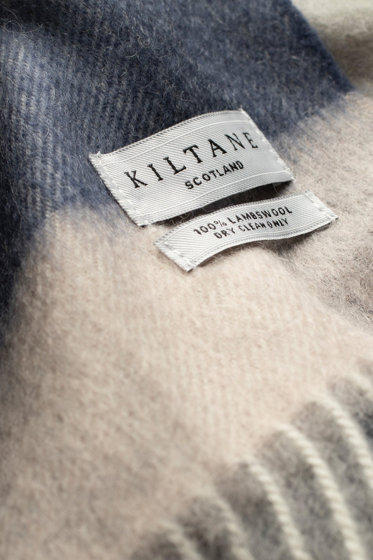 Close-up of Kiltane Scotland label on 5 Square Check Lambswool Scarf in Swiss Coffee showing 100% lambswool care tag