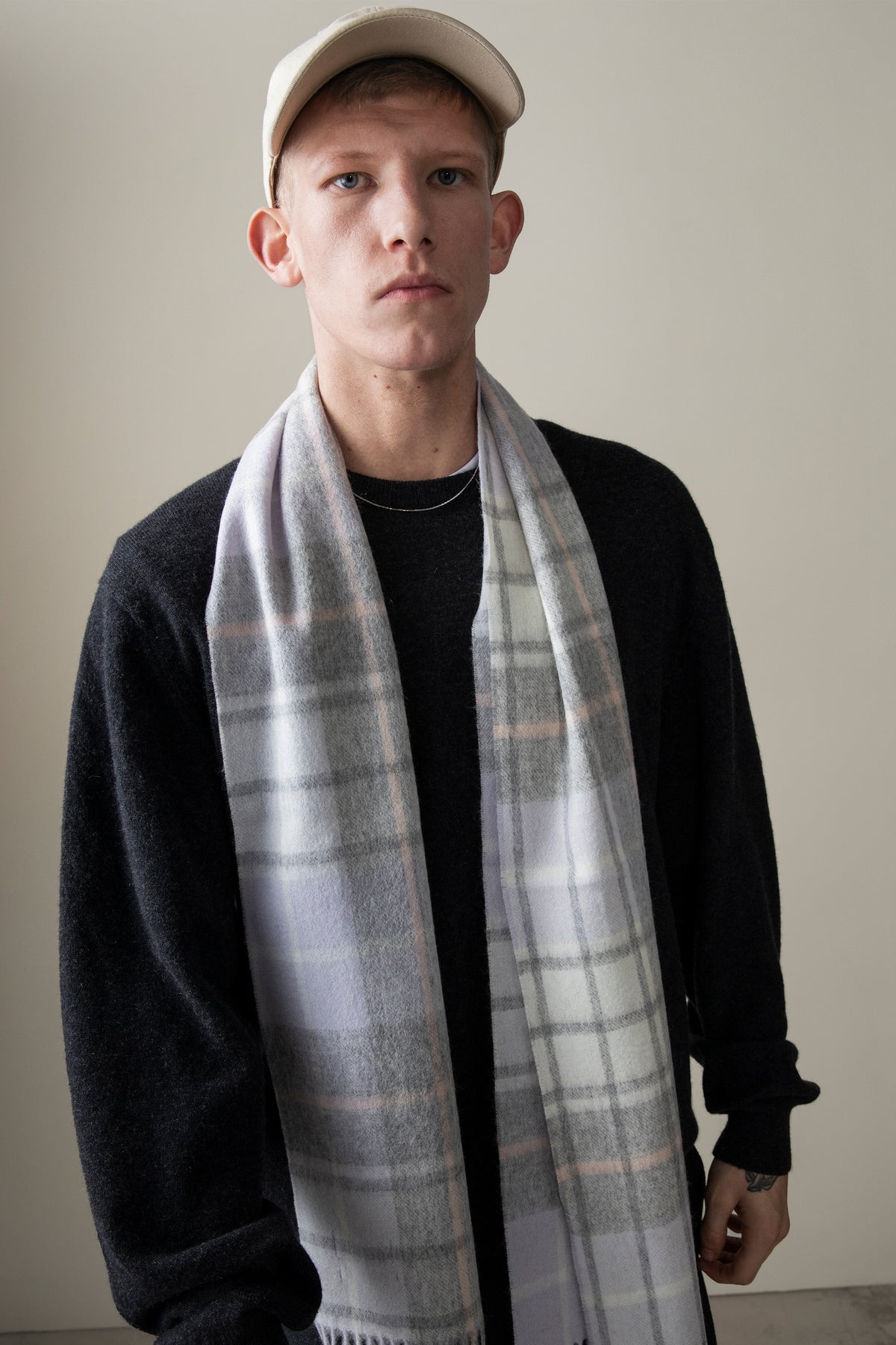 Model wearing the Contemporary Check Lambswool Scarf in Moonshadow draped over a black sweater, showing the grey and blush plaid pattern