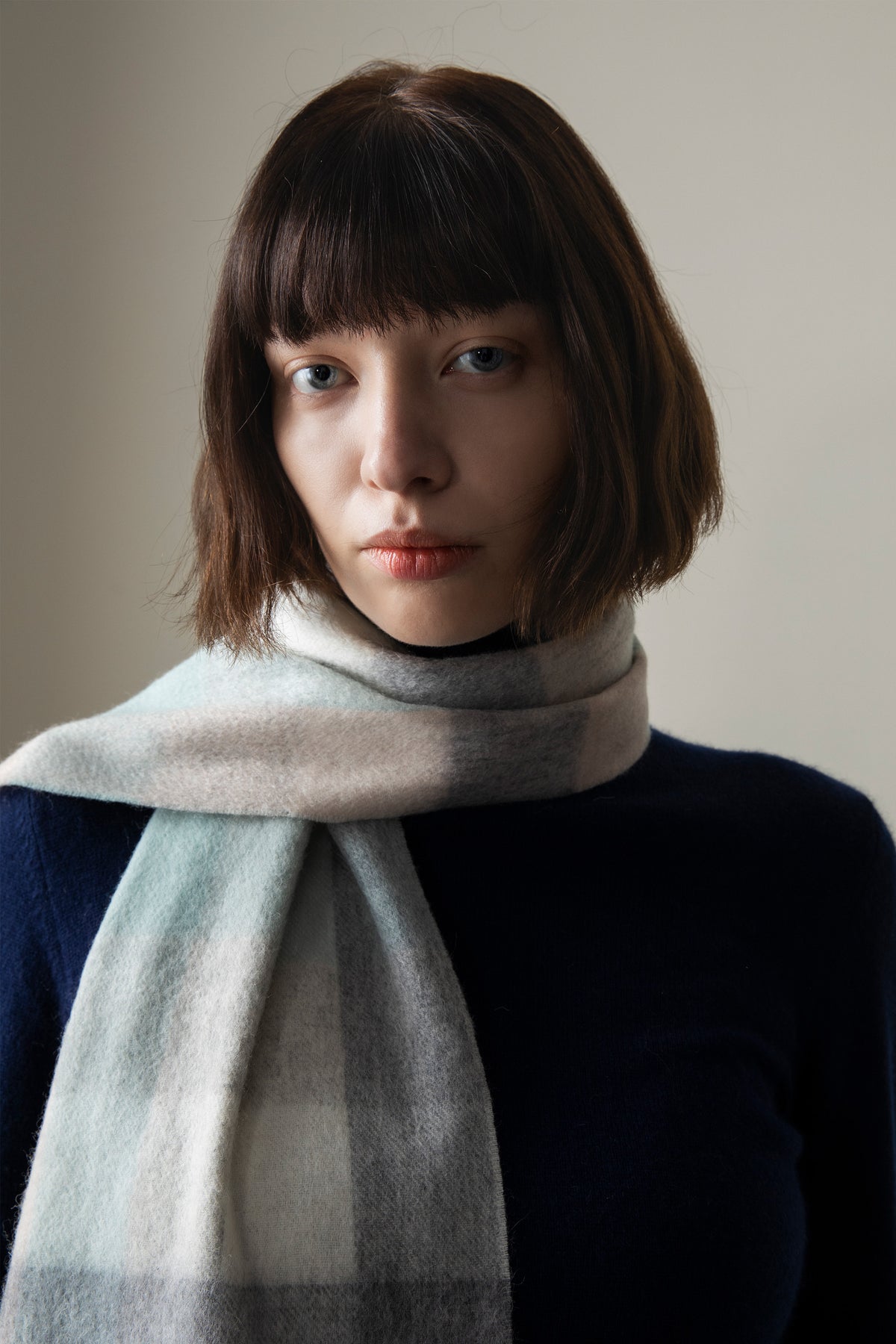5 Square Check Lambswool Scarf in Brume worn wrapped once around the neck, showing soft green and grey check pattern