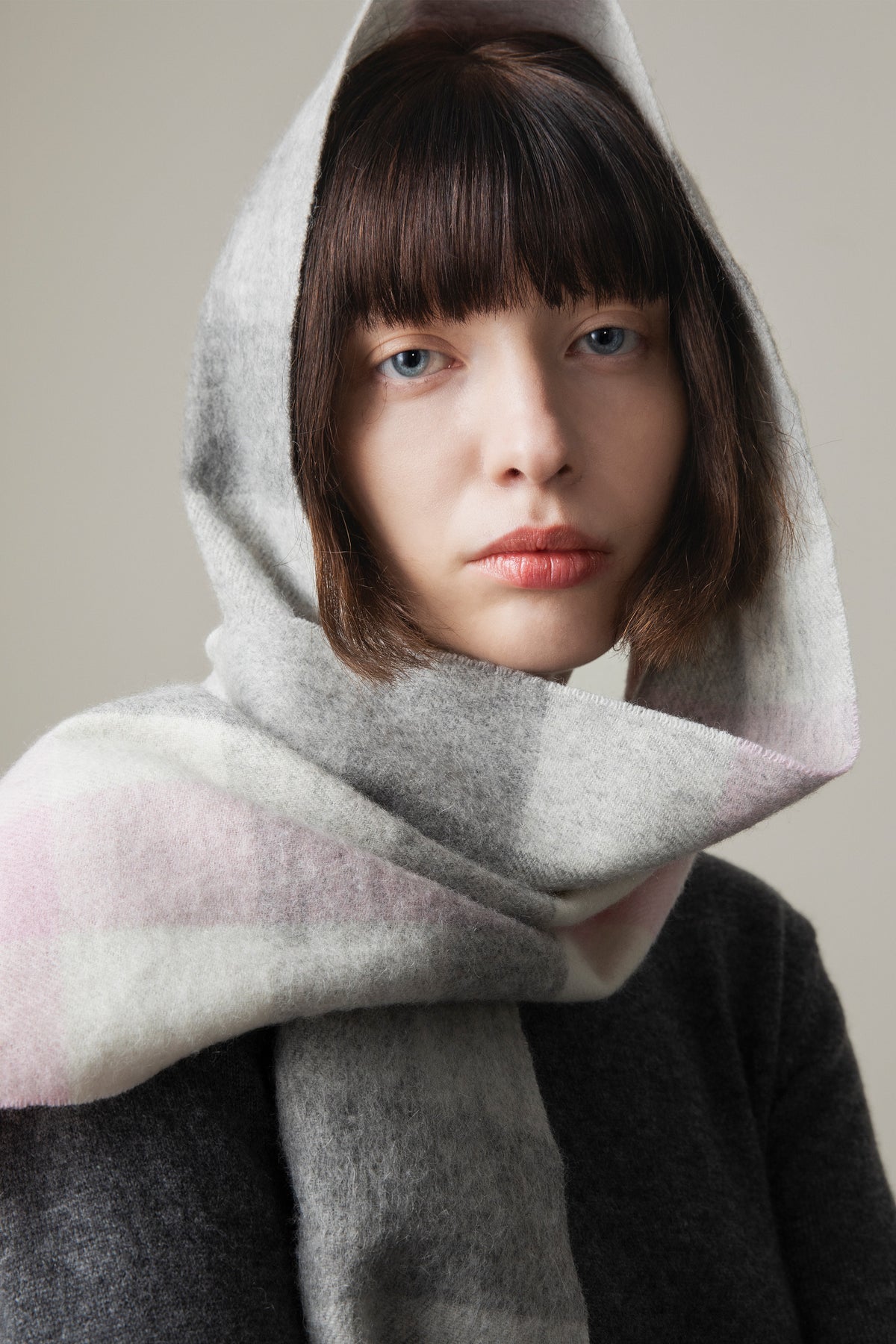 5 Square Check Lambswool Scarf in Cherub worn as a headscarf, showing soft grey and pink check pattern draped around the neck