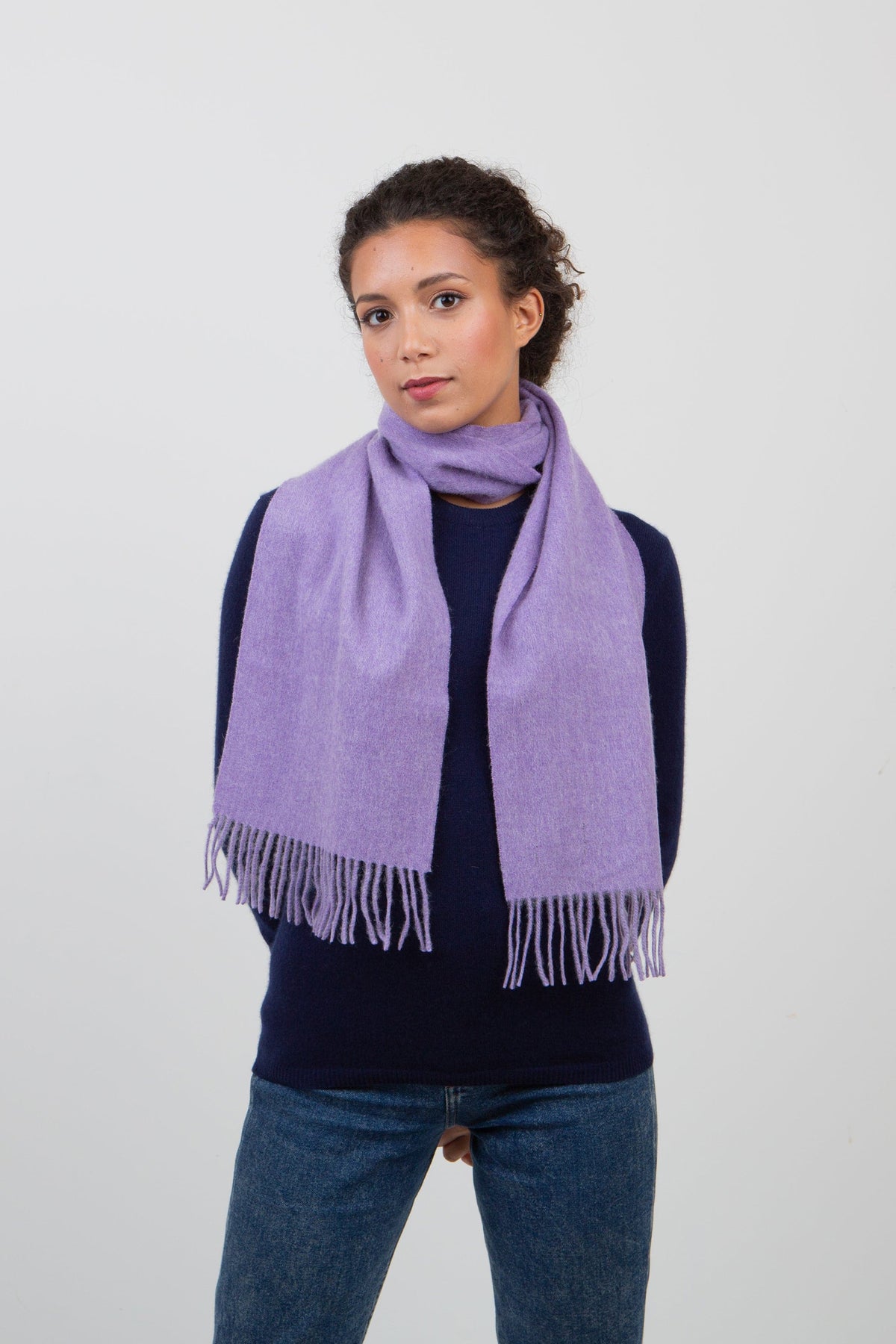 Solid Lambswool Scarf in Heather, a soft lavender-purple wool scarf with fringed ends, worn loosely wrapped around the neck