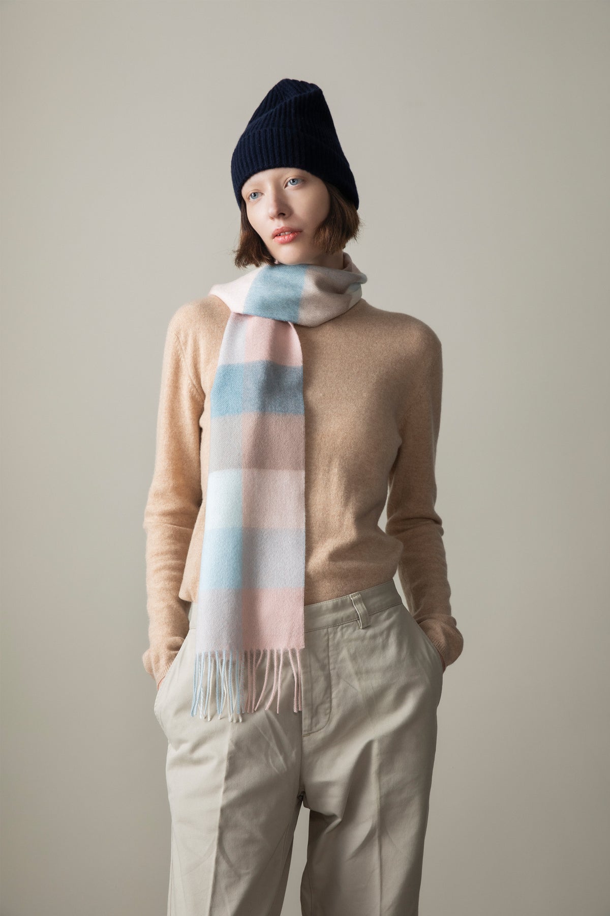 3 Square Check Lambswool Scarf in Seashell worn looped around the neck, showing pastel pink and blue check pattern with fringed ends