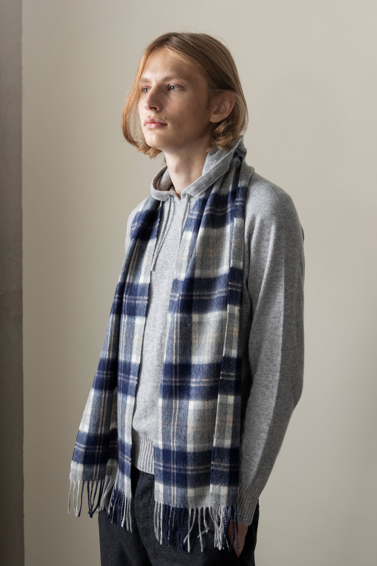 Heritage Tartan Lambswool Scarf in Silver Bannockbane worn draped over a grey hoodie, featuring navy and cream plaid with fringed ends