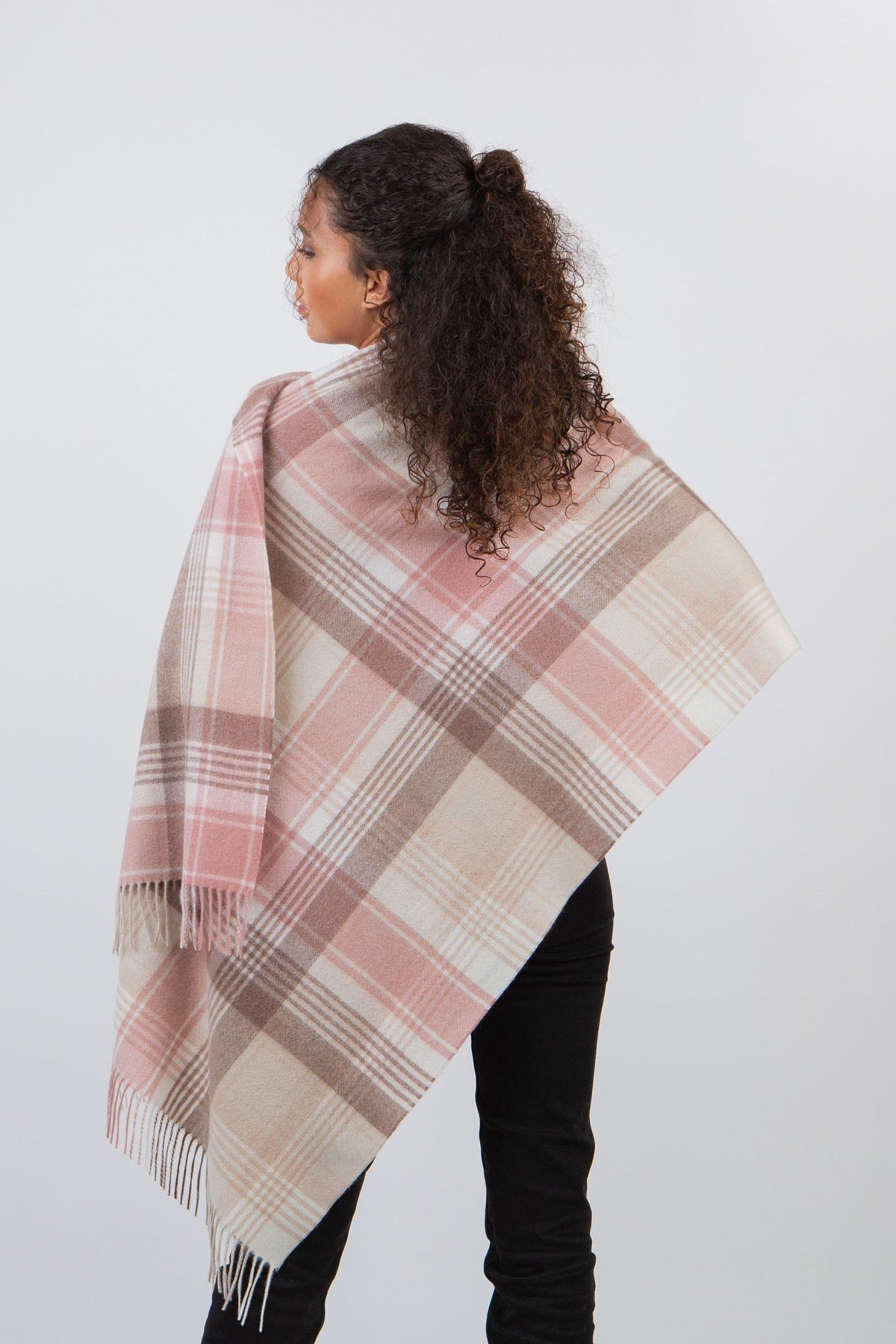 Back view of model wearing Repeat Edge Lambswool Stole in Natural, showing pink and cream plaid pattern with fringed edges