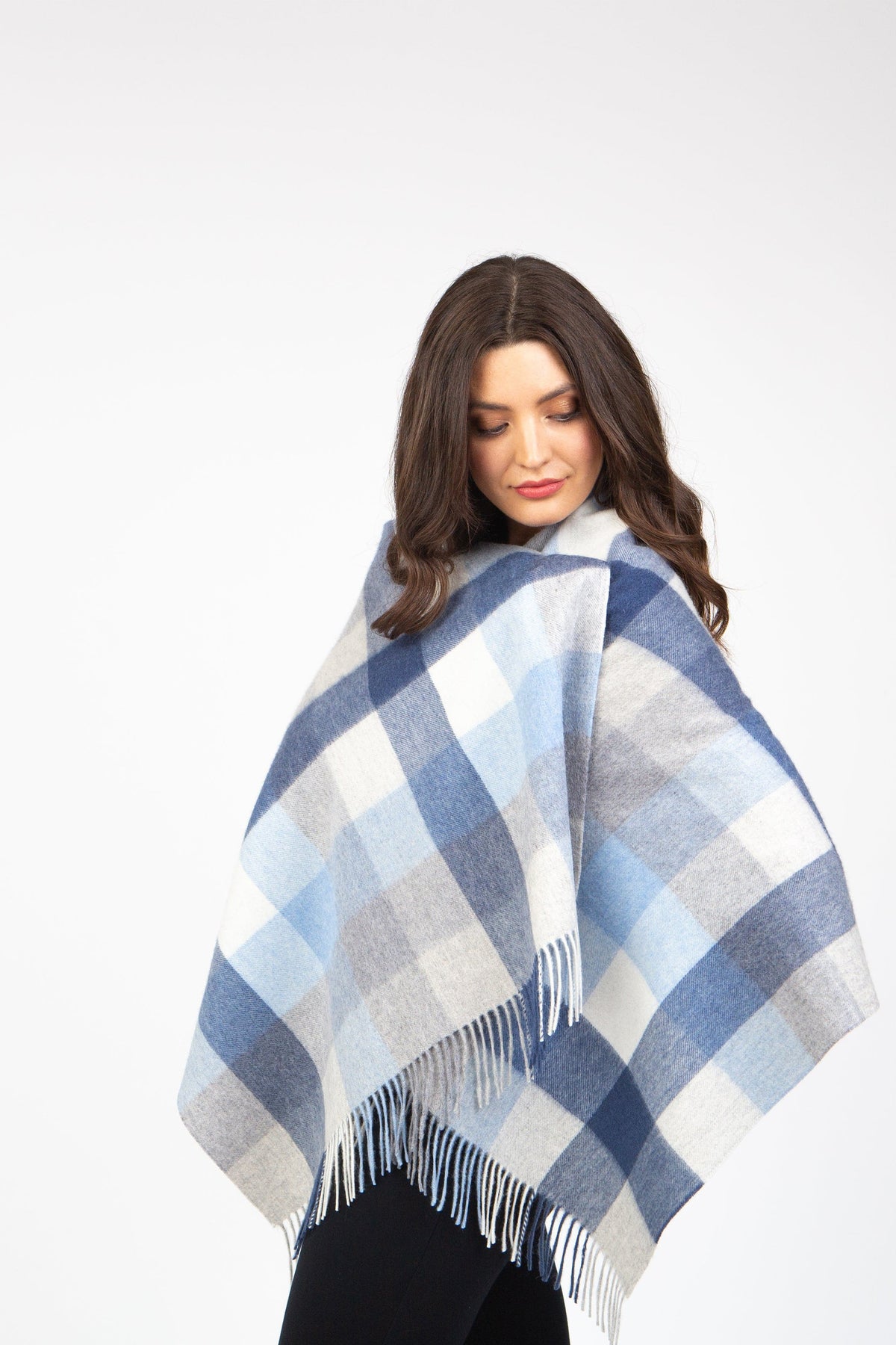 Model wearing the 5 Square Check Lambswool Stole in Glacier draped as a poncho, showing blue and grey plaid pattern with fringed hem