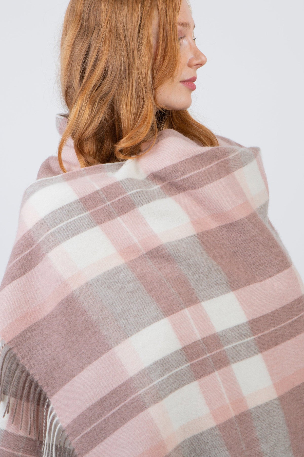 Contemporary Check Lambswool Stole in Cameo draped over shoulders, showing pink, grey, and cream plaid pattern with fringed edge
