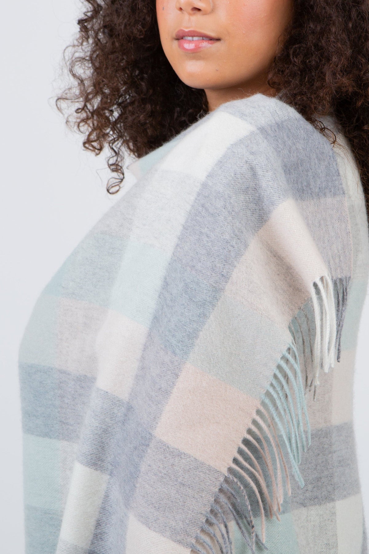 Close-up of 5 Square Check Lambswool Stole in Brume draped over shoulder, showing soft plaid pattern and fringed edge detail