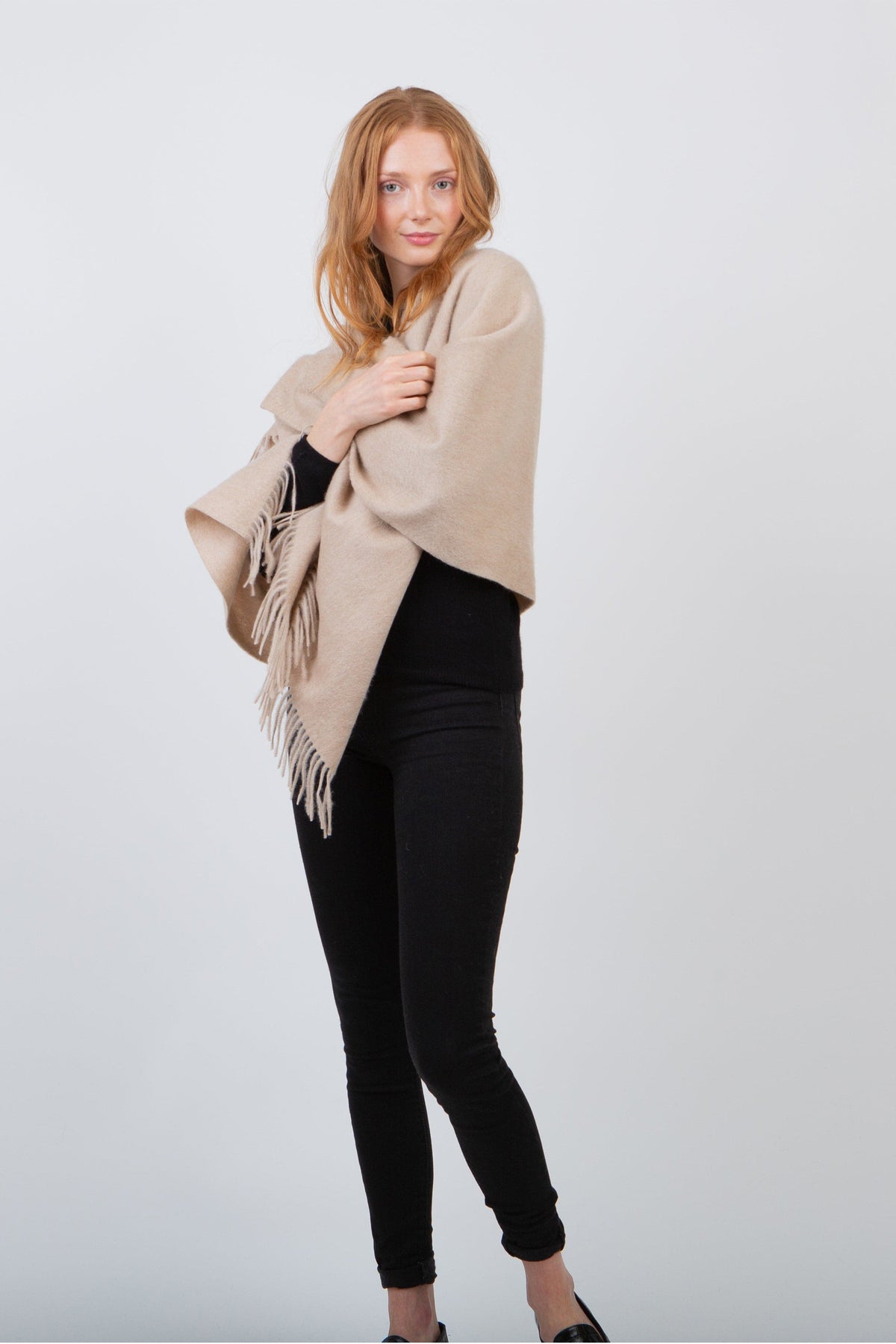 Solid Lambswool Stole in Vicuna, a soft beige fringed wrap draped over the shoulders, styled with a black outfit