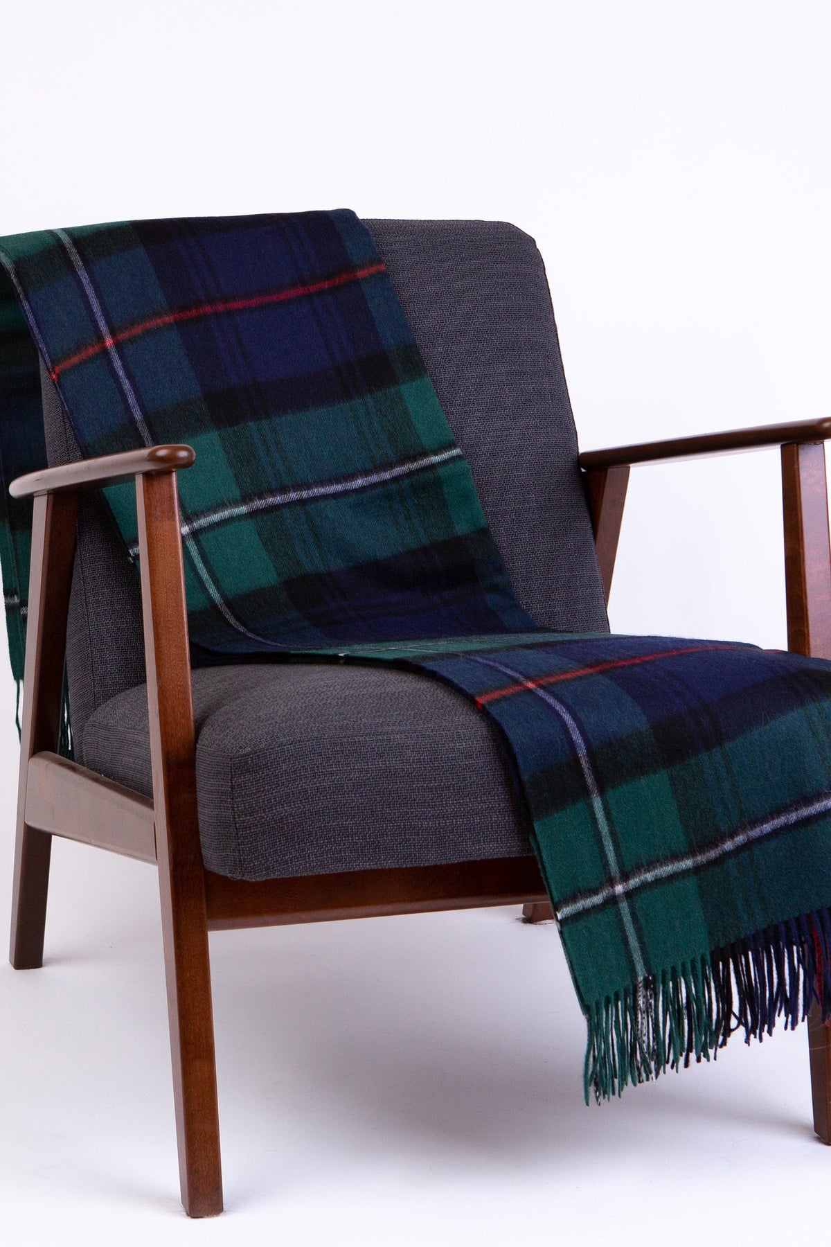 Lambswool Throw - Mackenzie in green and navy tartan draped over a mid-century armchair, showing fringed edge detail