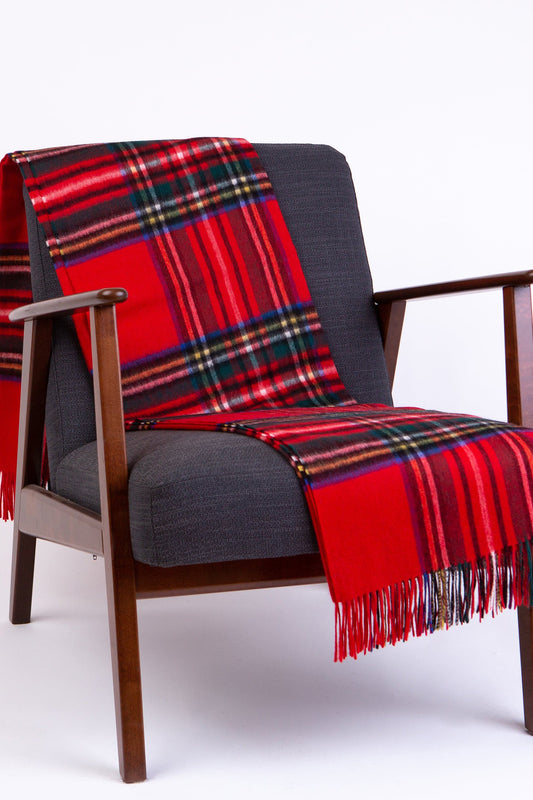 Lambswool Throw in Royal Stewart tartan with red, green, and blue plaid pattern and fringed edges, draped over a chair