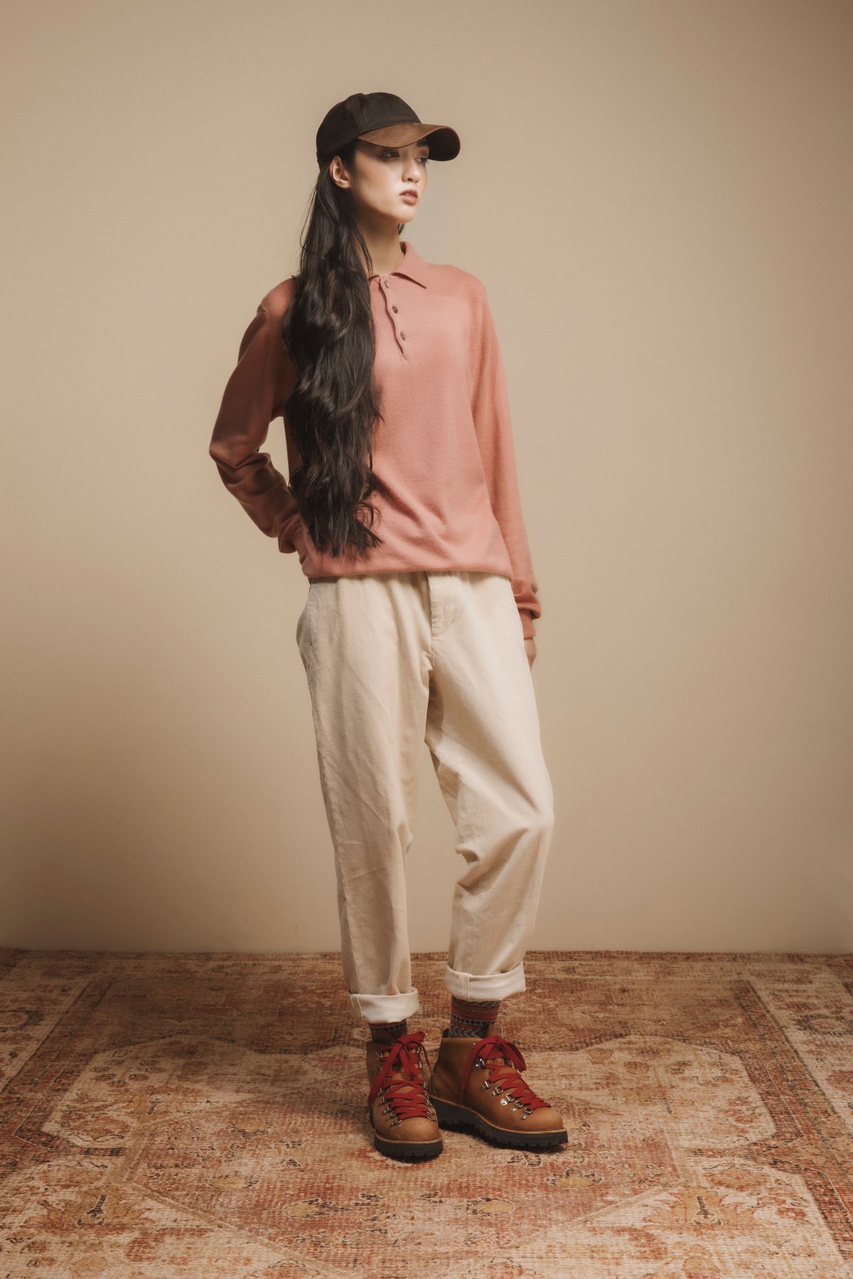 Wax Baseball Cap in brown worn by model styled with pink polo sweater, cream trousers, and hiking boots