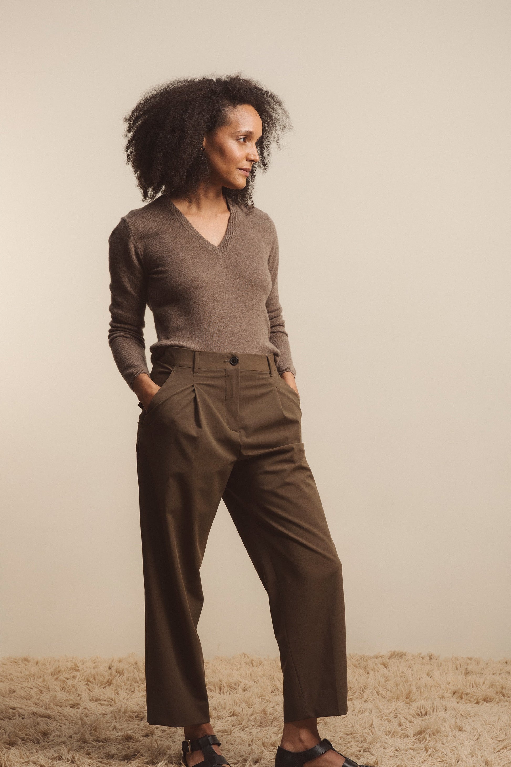 Women's Cashmere V Neck Jumper in Squirrel, a warm taupe knit with ribbed cuffs and hem, styled with olive pleated trousers