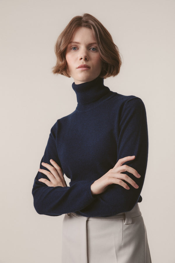 Model wearing Women's Cashmere Polo Neck Jumper in Cosmos navy blue, front view with arms crossed showing slim fit and soft knit texture